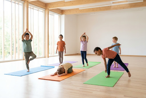Diverse children happily practicing simple yoga poses on colorful mats in a bright, airy school hall